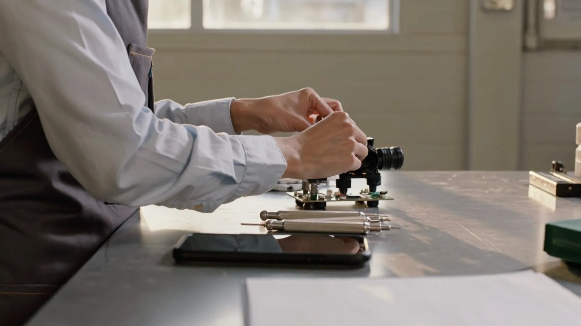An engineer at her workbench, working on a prototype, as her phone lights up with a new investor commitment